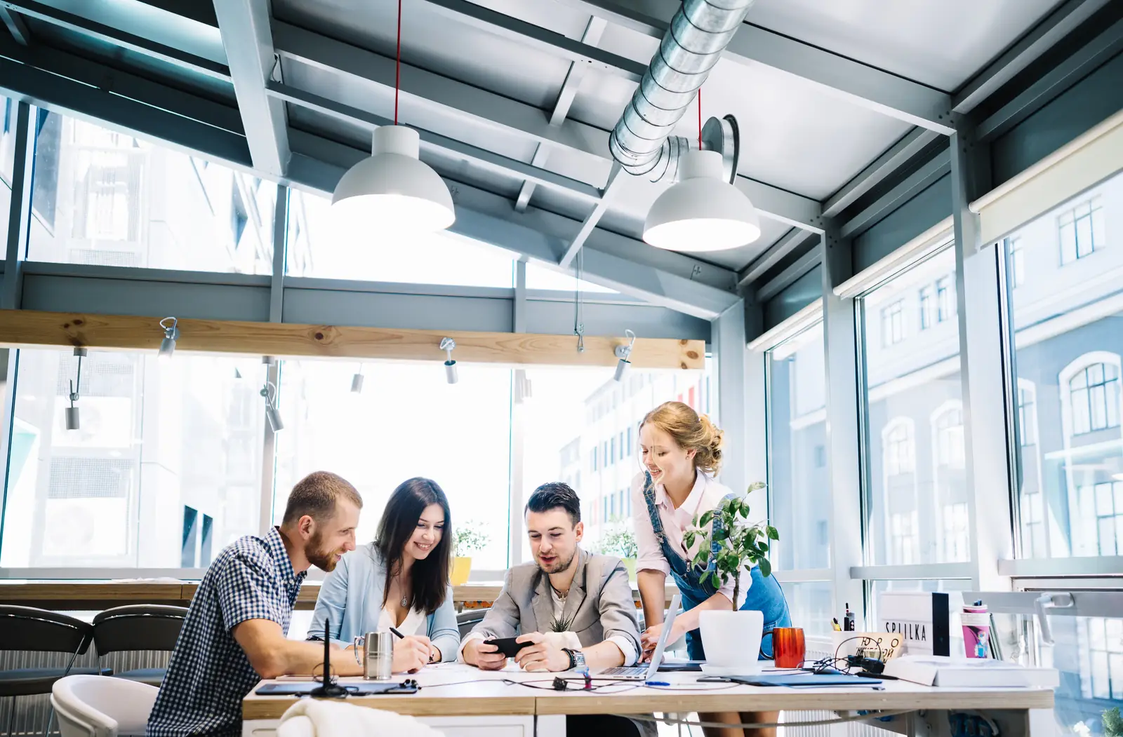 quatre collègues autour d'une table de travail, l'un d'eux montre son téléphone
